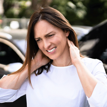 Woman standing outside next to car accident holding the back of her neck with whiplash in Clifton NJ