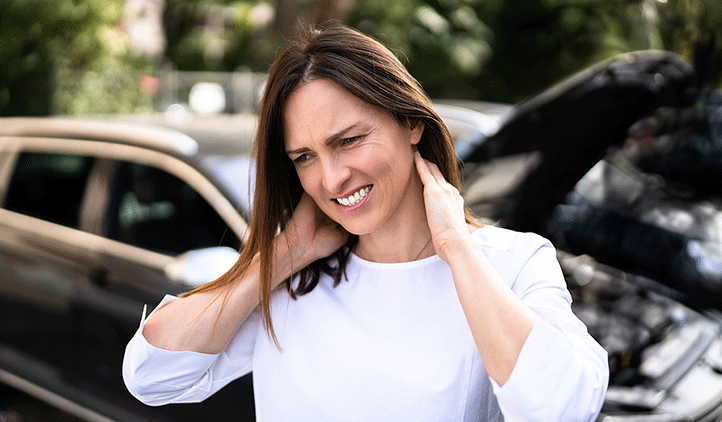 Woman standing outside next to car accident holding the back of her neck with whiplash in Clifton NJ